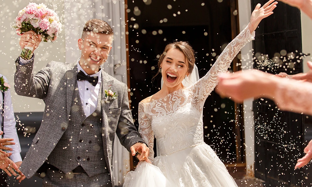 celebratory rice being tossed at young happy couple dressed in wedding attire