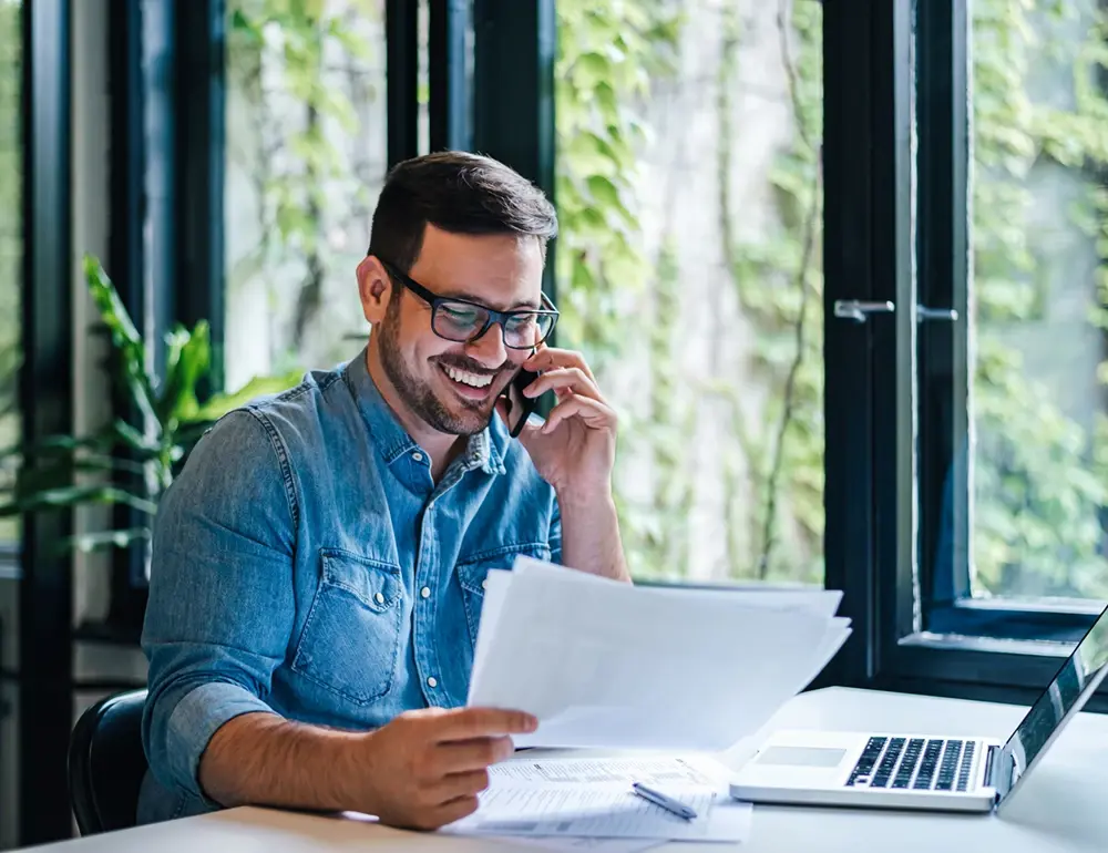 Smiling man with a papers in hand on phone