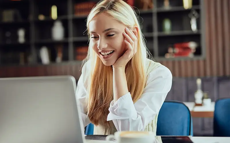 Female blogger dressed smart casual sitting in cafeteria and using laptop