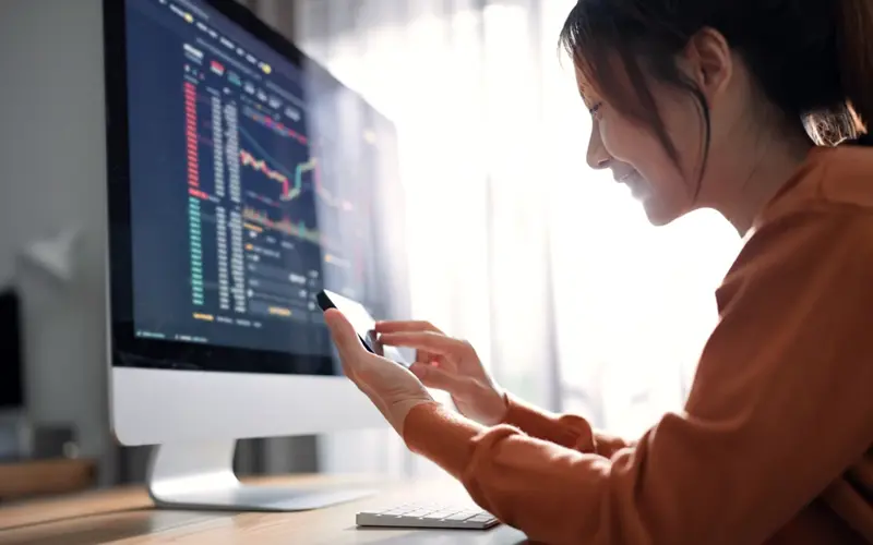 Woman using phone next to computer