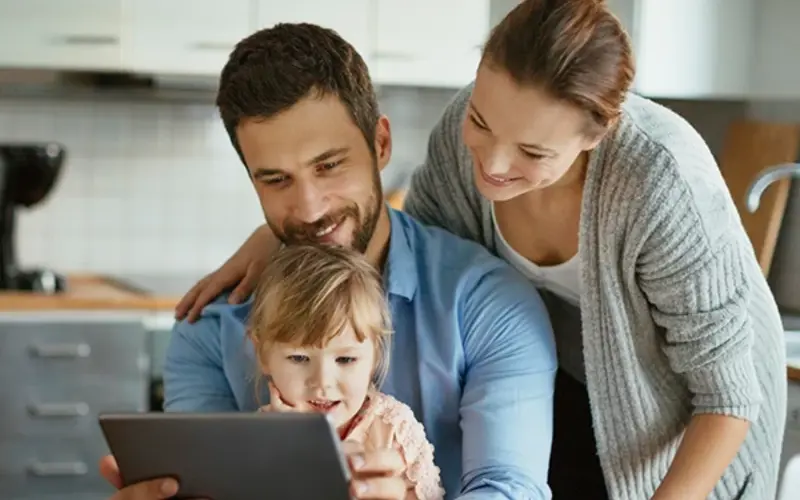 Happy parents using tablet with small daughter at home 