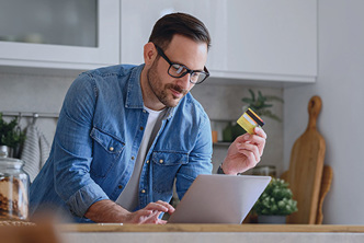 Image of a man using a laptop and holding a credit card.