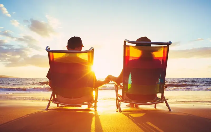 older couple holding hands while sitting on a beach