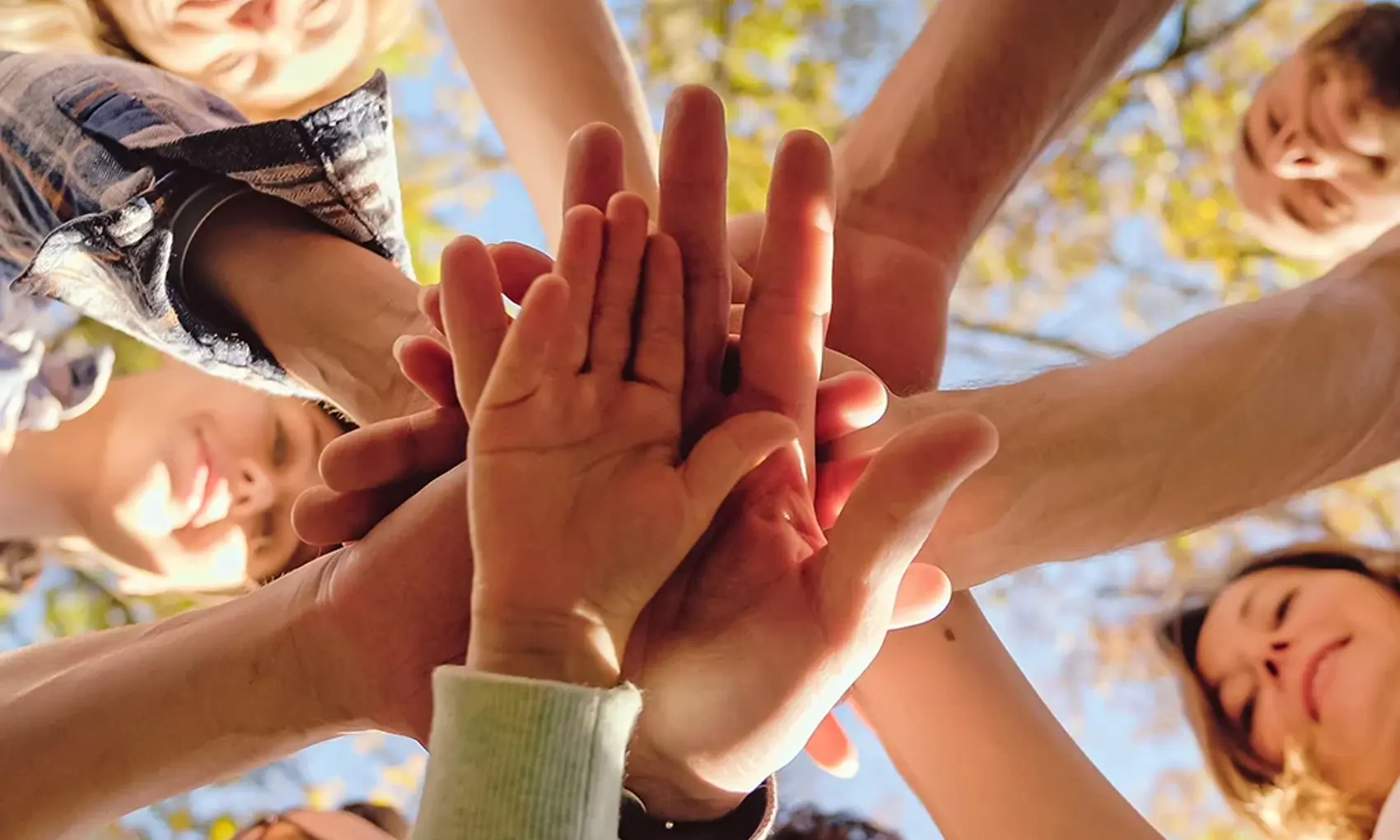 Close up from below on men and women with kid putting hand on hand in circle and making gesture of cooperation and coworking. 