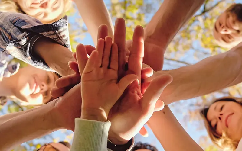 Close up from below on men and women with kid putting hand on hand in circle and making gesture of cooperation and coworking. 