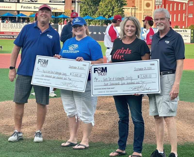 Two organizations at a ballpark holding oversized donation checks next to FMT employees