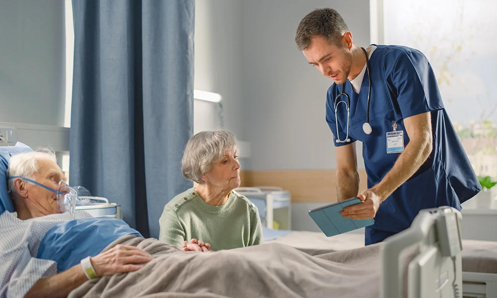 older woman looking at paperwork while incapacitated husband is in hospital bed