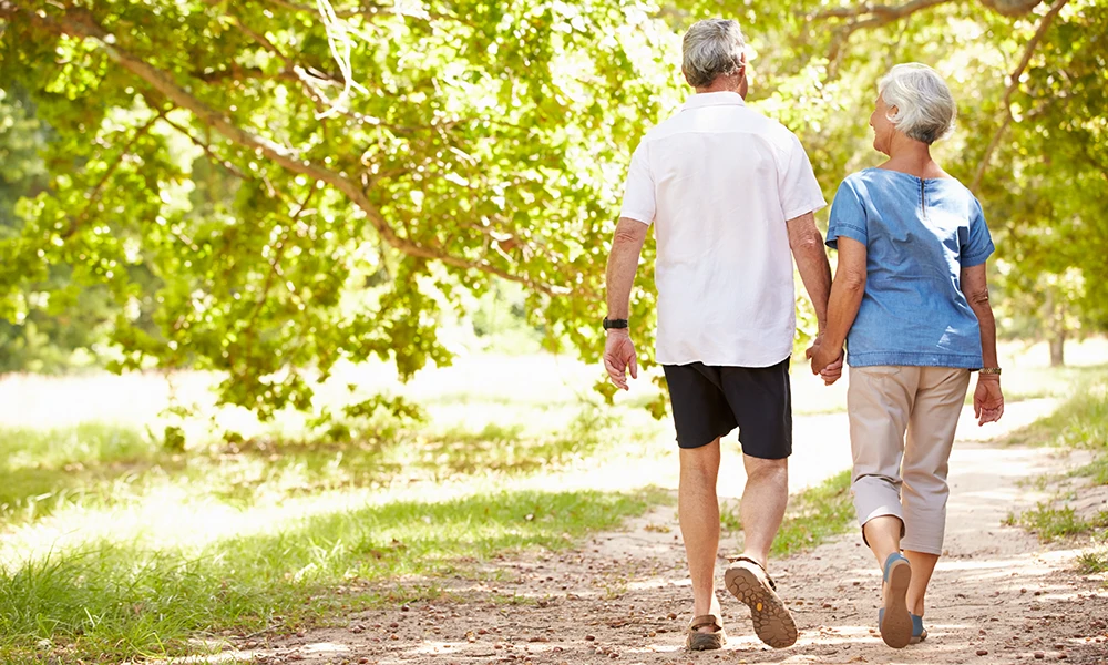 older adults holding hands while walking on a path 