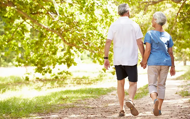 older adults holding hands while walking on a path 