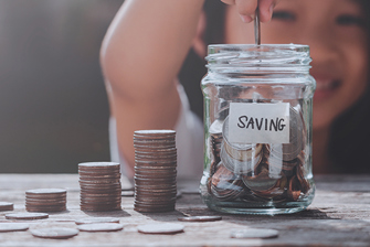 A young girl putting a coin into a jar of coins labeled "Saving".