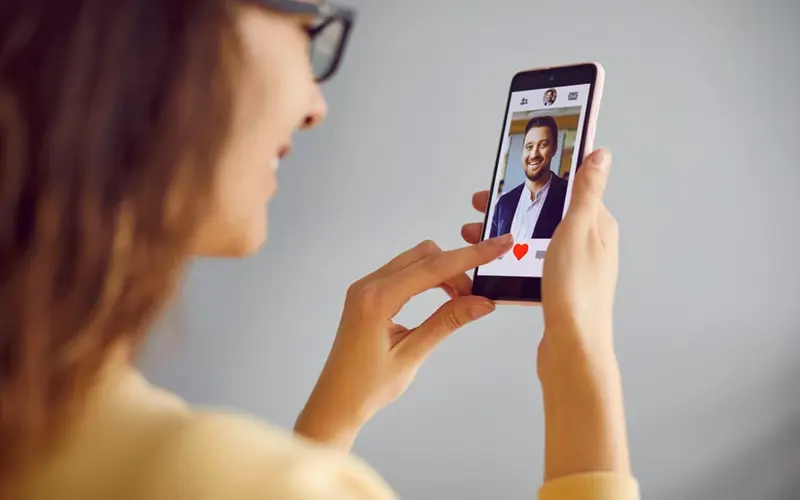 woman smiling at a picture of man on her phone with a heart icon 