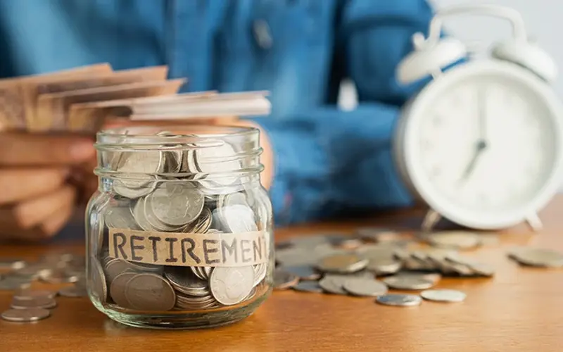 glass jar of coins labelled retirement with clock in background