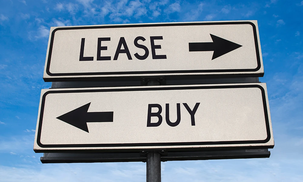 two street signs that point in opposing directions and read Lease versus Buy 