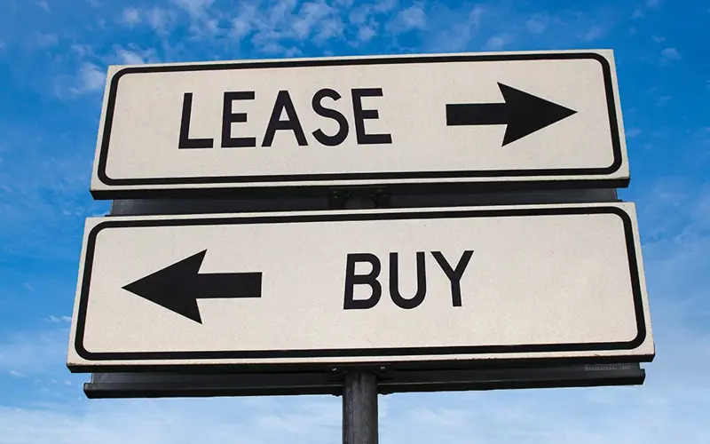 two street signs that point in opposing directions and read Lease versus Buy 